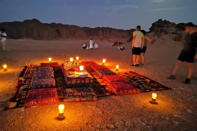 Candlelit desert dinner with cushions and rugs at dusk