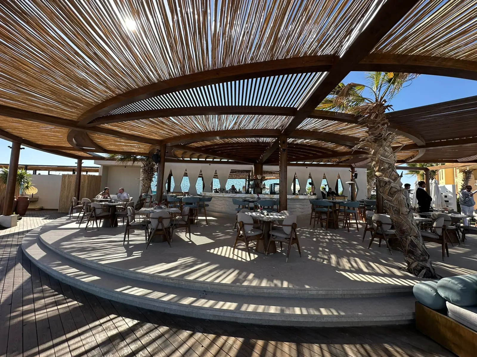 Circular seating area under a slatted wooden roof at the beach venue